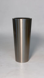 A brushed stainless steel cylinder, likely a tumbler, vase, or planter, standing upright on a light gray surface against a neutral gray background.