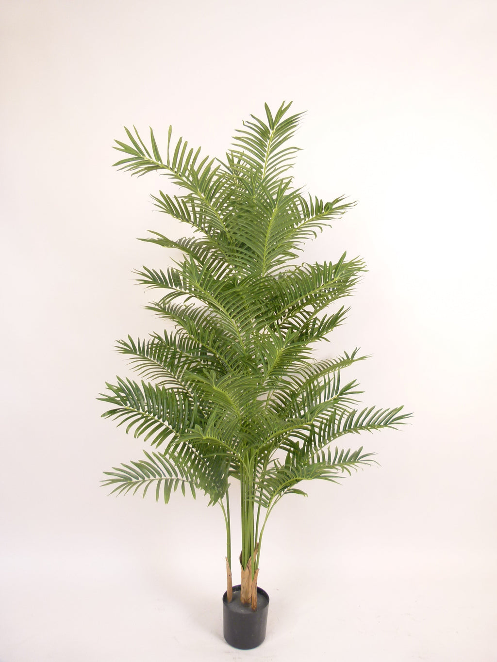 An indoor artificial palm plant in a black plastic pot, photographed against a plain white background.