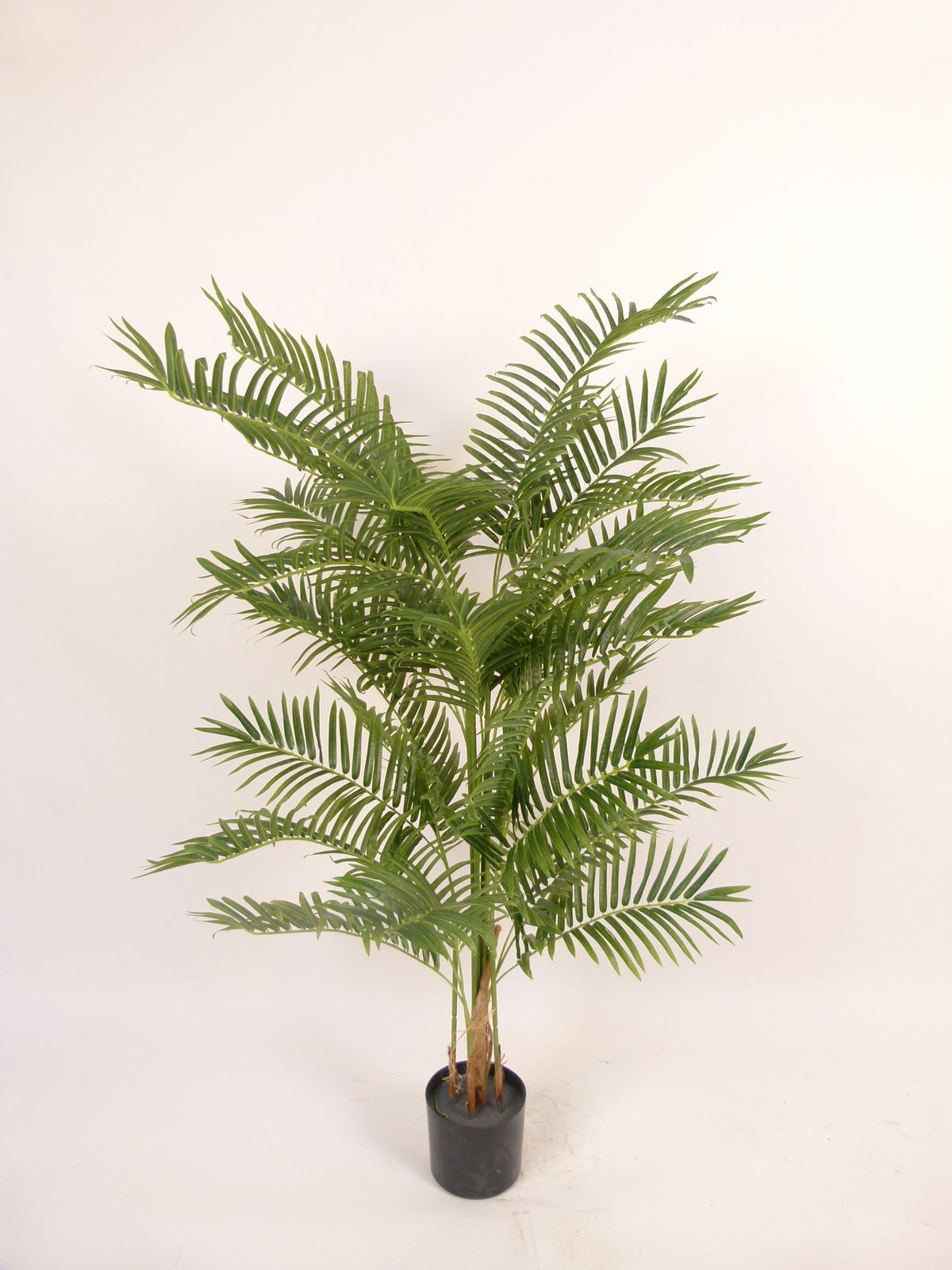 An artificial green palm plant in a small black plastic nursery pot, photographed against a plain off-white background.