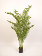 Green artificial palm fronds in a black plastic pot, photographed against a plain off-white background.